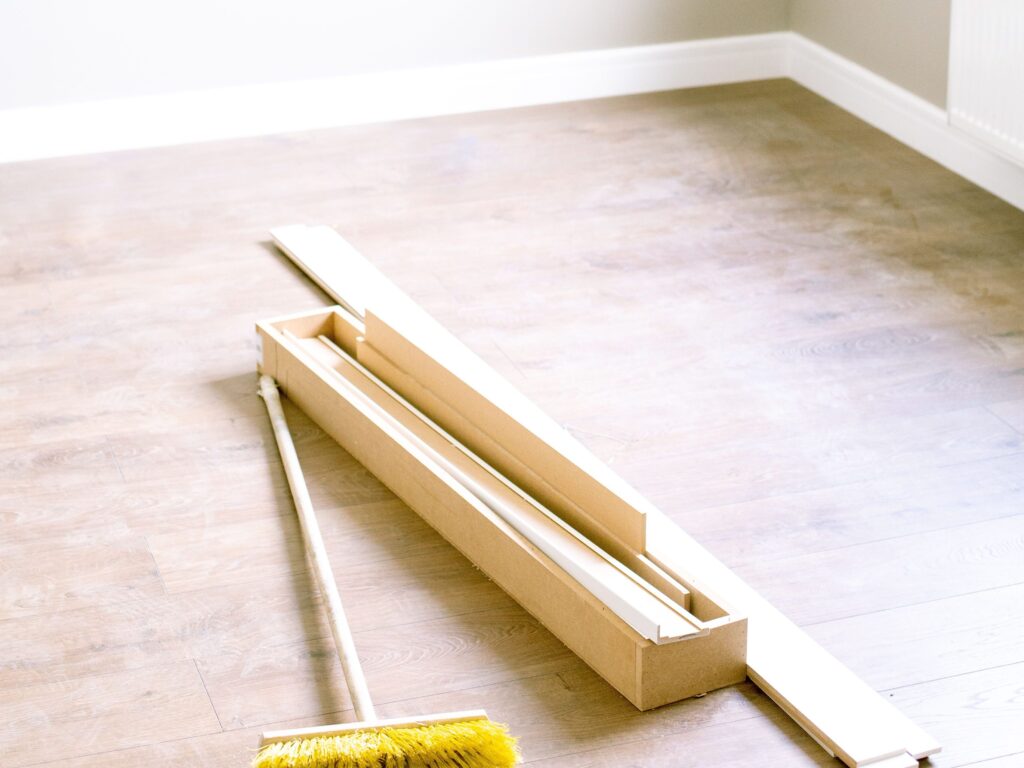 An empty room with wood planks and a broom, ready for renovation.